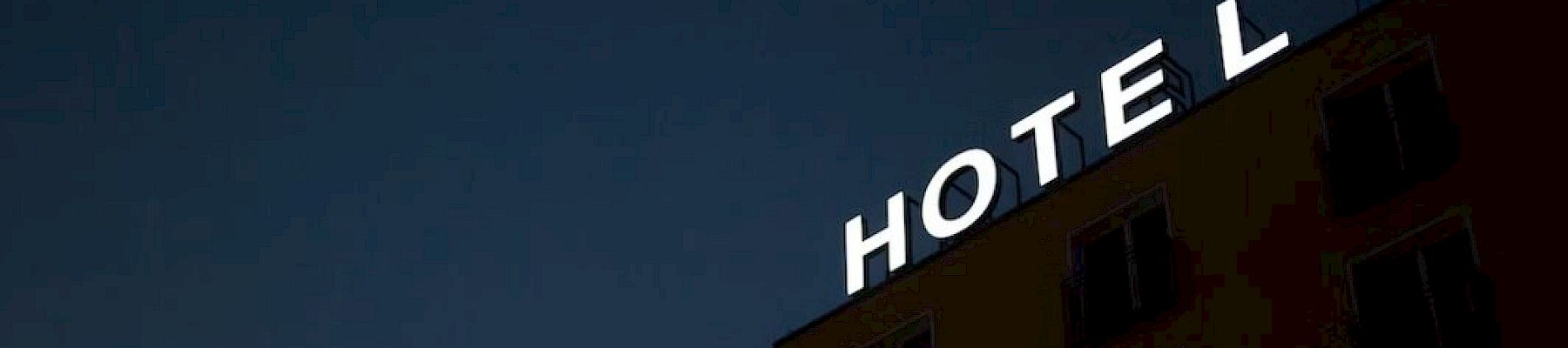 A hotel building with missing lit-up sign letters against a night sky, showing the word "HOTEL" with the letter "E" missing.