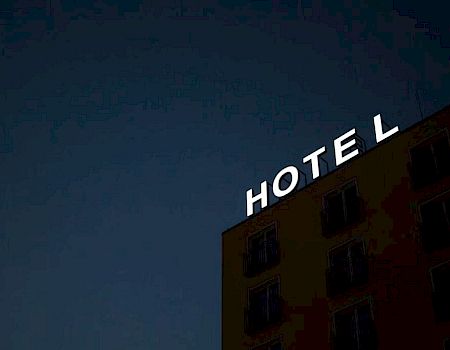 A hotel building with missing lit-up sign letters against a night sky, showing the word "HOTEL" with the letter "E" missing.