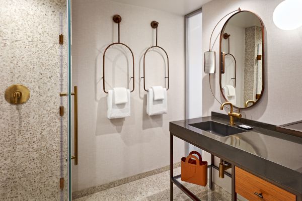 A modern bathroom with a black countertop, gold fixtures, terrazzo tiles, towel holders with towels, and an oval mirror.