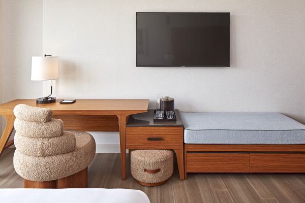 A modern room with a wooden desk, a stylish chair, a mounted TV, a small table with drinks, and integrated seating.