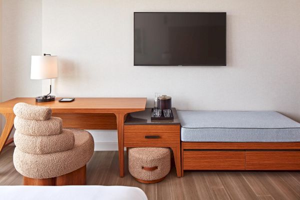 A modern room with a wooden desk, cozy chair, smart TV, and seating area. Simple, elegant design with neutral tones throughout.