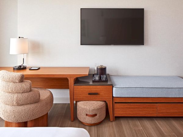 A modern room with a wooden desk, cozy chair, smart TV, and seating area. Simple, elegant design with neutral tones throughout.
