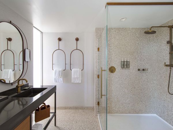 A modern bathroom with glass shower, terrazzo tiles, black sink countertop, and metal fixtures, featuring towels and bath products.