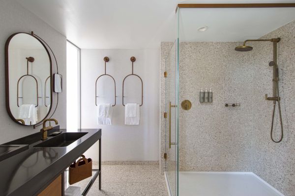 A modern bathroom with a glass shower, terrazzo tiles, black countertop, and brass fixtures.