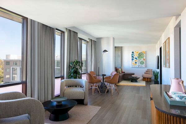 A modern living space with large windows, comfortable seating, hardwood floors, and a colorful painting on the wall.
