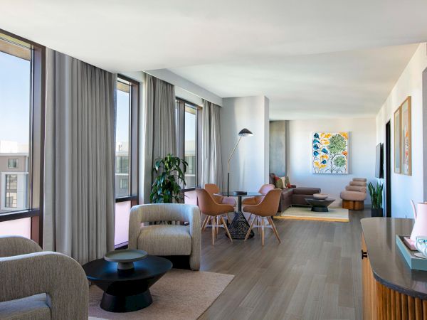 A modern living space with large windows, comfortable seating, hardwood floors, and a colorful painting on the wall.