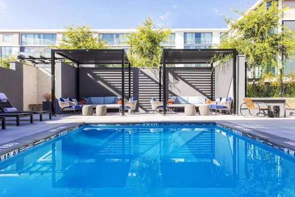 A modern outdoor pool area with cabanas, seating, and lush greenery. The area appears to be designed for relaxation and comfort.