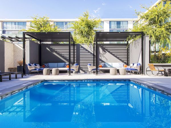 A modern outdoor pool area with cabanas, seating, and lush greenery. The area appears to be designed for relaxation and comfort.