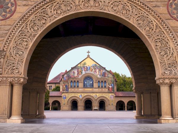 A detailed archway frames a colorful, decorated building with a cross on top, creating a symmetrical view of architectural beauty.