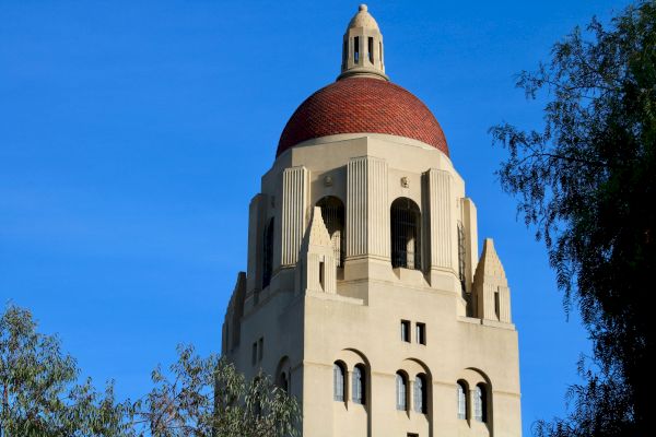 A tall building with a red-tiled dome and arched windows, framed by blue sky and trees.