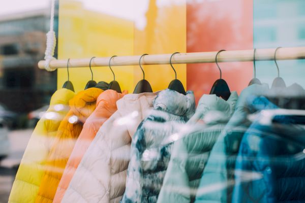 A display of colorful jackets on hangers is shown through a shop window with reflections.