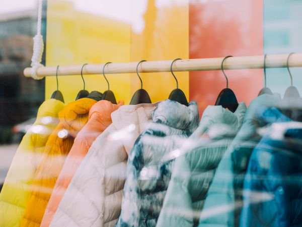 A display of colorful jackets on hangers is shown through a shop window with reflections.
