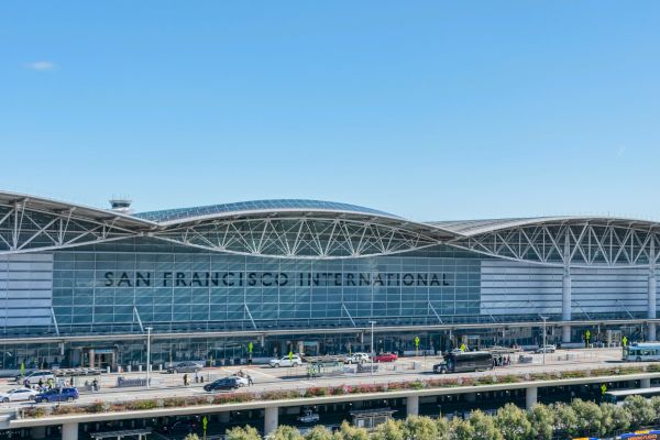 The image shows the exterior of San Francisco International Airport, featuring modern architecture and vehicles in front of the terminal.
