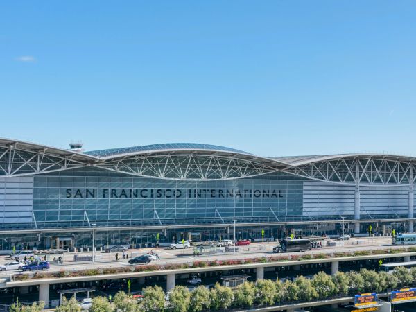 The image shows the exterior of San Francisco International Airport, featuring modern architecture and vehicles in front of the terminal.
