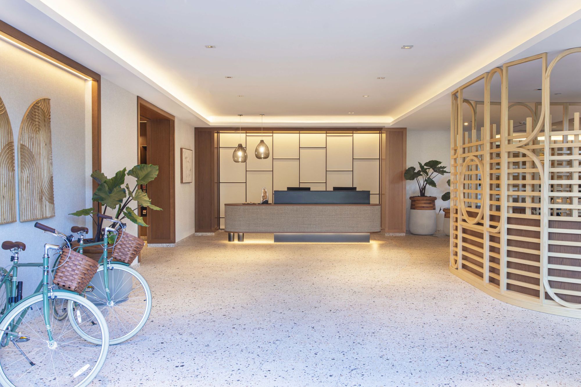 A modern reception area with a desk, decorative plants, bikes, and stylish lighting, featuring minimalist design elements.