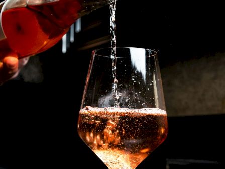 A person pours rosé wine into a glass, with bubbles visible and a dark background.