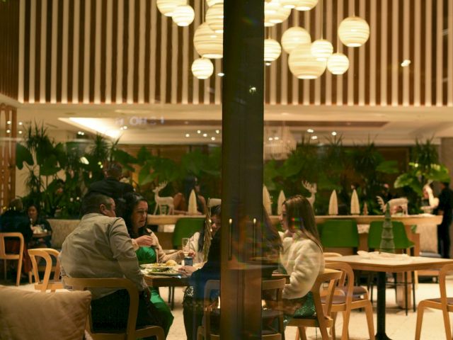 People sit around tables in a stylish restaurant with modern lighting and a cozy fire pit.