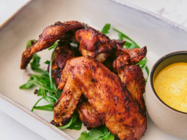 Grilled chicken wings on arugula with a side of yellow dipping sauce, served in a rectangular dish.