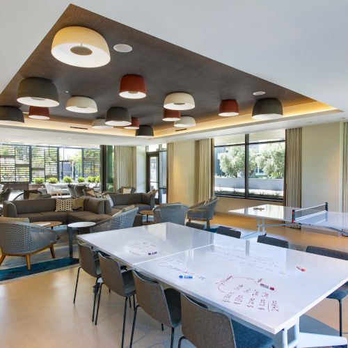 Modern lounge with comfortable seating, a ping-pong table, and writable tables, featuring unique overhead lighting.