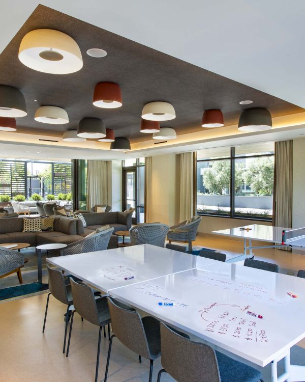Modern lounge with comfortable seating, a ping-pong table, and writable tables, featuring unique overhead lighting.
