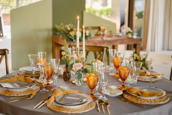 A beautifully set dining table with plates, yellow glasses, candles, and floral centerpieces, perfect for a formal or festive gathering.