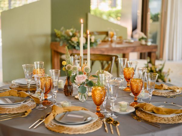 A beautifully set dining table with plates, yellow glasses, candles, and floral centerpieces, perfect for a formal or festive gathering.