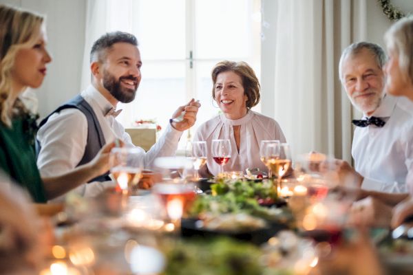 A group of people sitting around a table enjoying a festive meal, with wine glasses and candles creating a warm, cozy atmosphere.