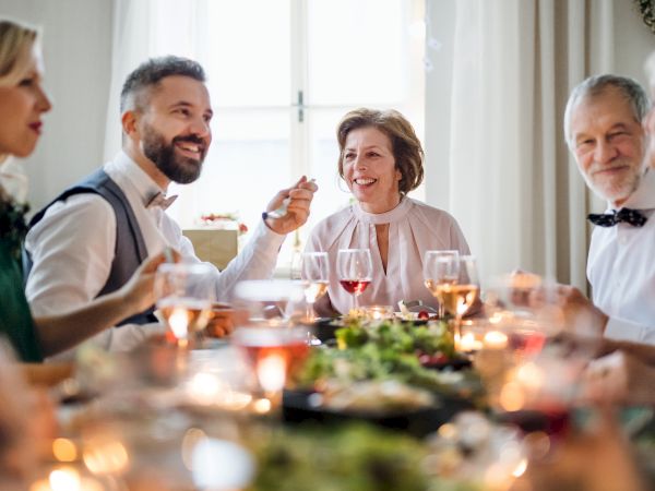 A group of people sitting around a table enjoying a festive meal, with wine glasses and candles creating a warm, cozy atmosphere.