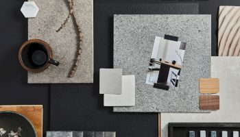 A flat lay of design materials, including textures, tiles, a cup, and a photo, arranged aesthetically on a dark surface.