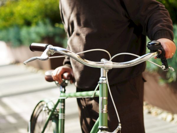 A man rides a green bicycle, leaning forward and gripping the handlebars on a sunny street.