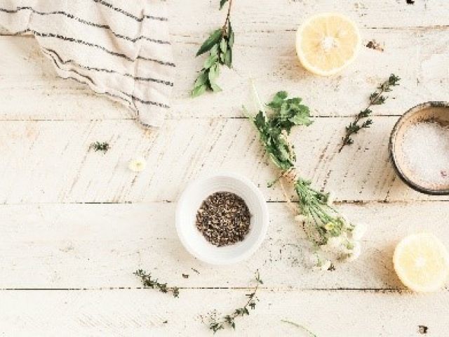 Herbs, lemon halves, a small bowl of salt, and a fabric cloth are arranged on a light wooden surface.