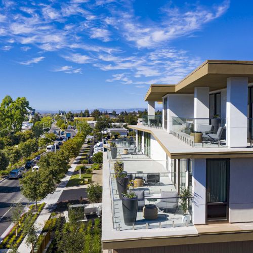 Modern building with large balconies overlooking a tree-lined street under a clear blue sky.