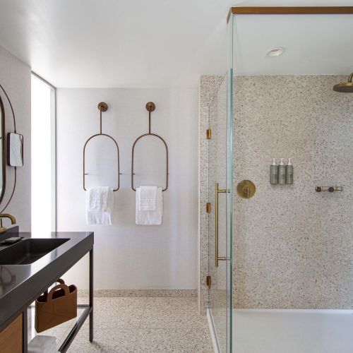 A modern bathroom features a black countertop, oval mirror, glass shower, and towel racks on textured walls with brass accents.