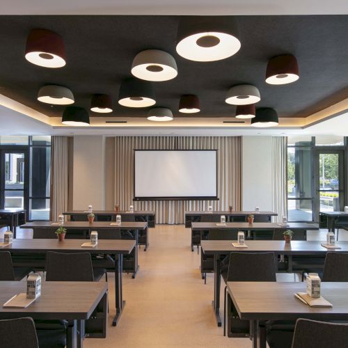 The image shows a conference room with tables, chairs, and a projector screen, set up for a meeting or presentation.