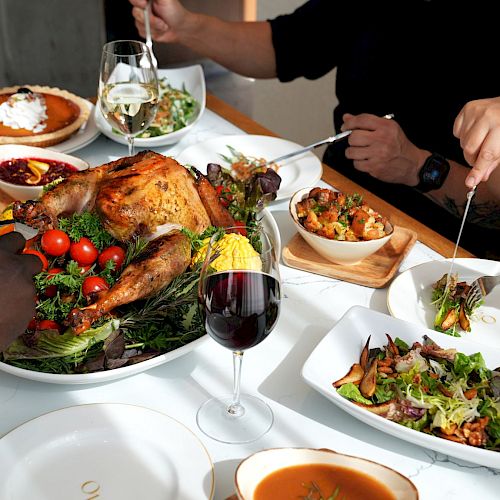A group sharing a meal with roast turkey, salads, and wine on a dining table.