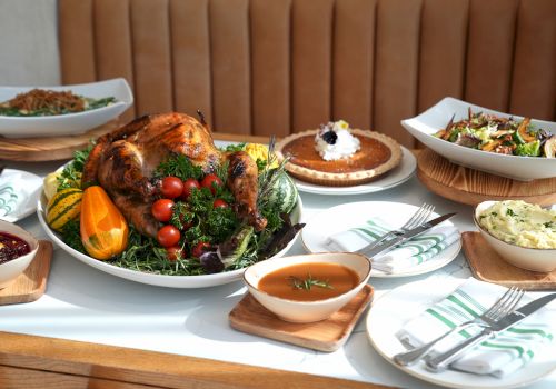 A table with a roasted turkey, pie, mashed potatoes, salad, and soup, elegantly arranged for a festive meal.