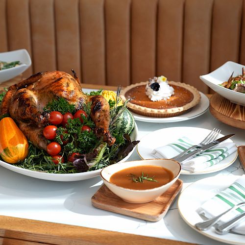 A table with a roasted turkey, pie, mashed potatoes, salad, and soup, elegantly arranged for a festive meal.
