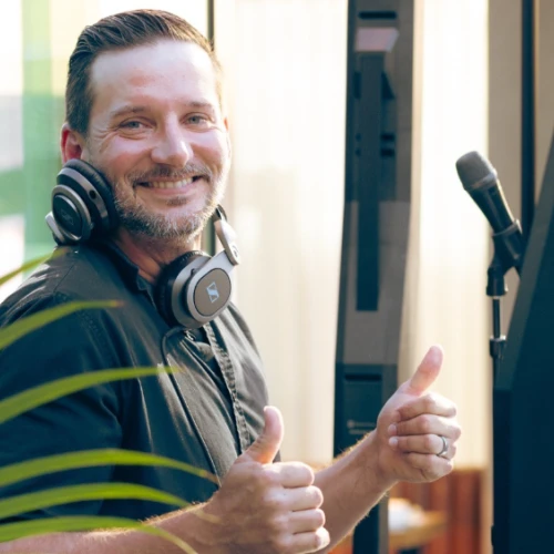 A person with headphones is smiling and giving thumbs up near a microphone and equipment.
