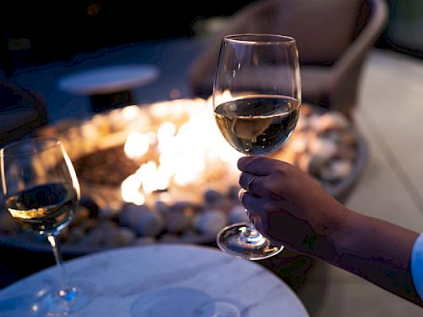 People clinking wine glasses around a lit fire pit at night, outdoor dining vibe. flavors, warmth, and conversation under dim lights.