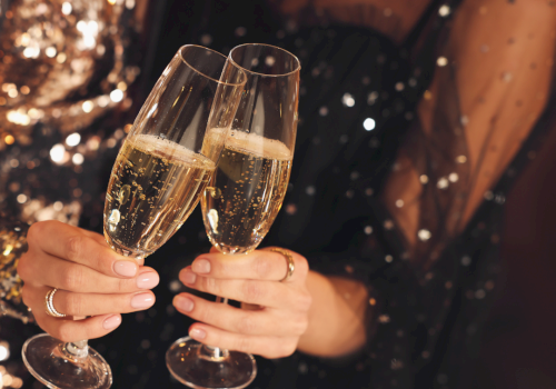 Two people clink champagne flutes in a festive, sparkly night celebration.
