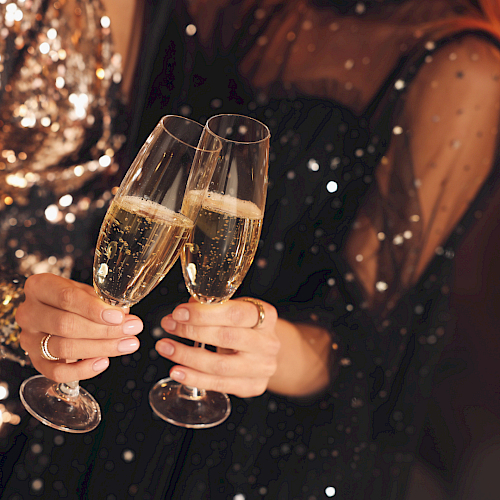Two people clink champagne flutes in a festive, sparkly night celebration.