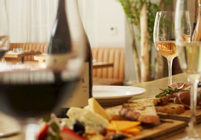 A cozy dinner scene with wine glasses, a cheese platter, and a bottle on a wooden table, ready for sharing, topped with warmth.