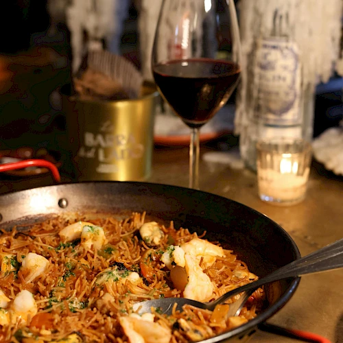 A sizzling skillet of pasta with mushrooms and herbs, a glass of red wine, candlelight, and cozy drinks in the background.