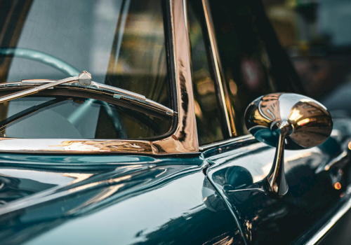 A close-up of a classic chrome car, showing polished blue bodywork, chrome side mirror, and vintage windscreen reflections, gleaming in light.