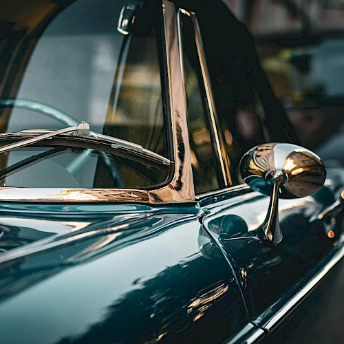 A close-up of a classic chrome car, showing polished blue bodywork, chrome side mirror, and vintage windscreen reflections, gleaming in light.