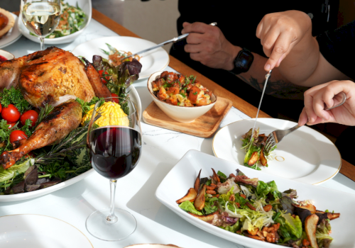 A family-style feast: roasted turkey, fresh salad, bowls of colorful sides, wine glass, and people sharing a plated meal at the table.