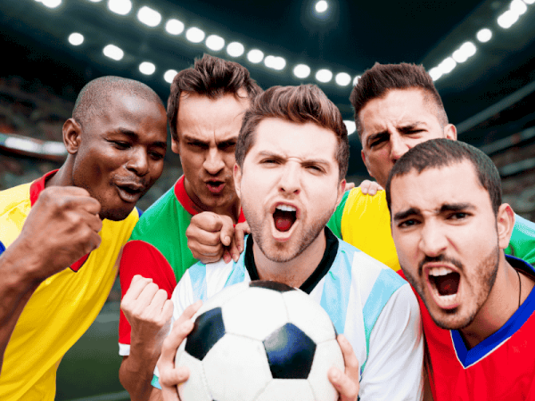 A diverse group of excited soccer players pose with a ball, cheering intensely at the stadium.