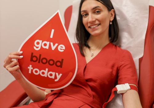 A woman in a red outfit sits in a red chair, holding a sign that says &ldquo;I gave blood today.&rdquo;